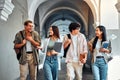 Four stylish modern smiling students are walking along the corridor of the university.