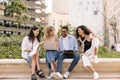 Four successful young interracial students discuss new topic among themselves relaxing sitting on campus.