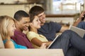 Four Teenagers Sitting On Sofa At Home Using Tablet Computer And Laptop Whilst Watching TV Royalty Free Stock Photo