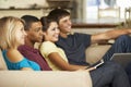 Four Teenagers Sitting On Sofa At Home Using Tablet Computer And Laptop Whilst Watching TV Royalty Free Stock Photo