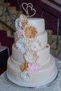 Four tiered wedding cake with pastel colored flowers, edible lace and pearls details, and heart-shaped topper Royalty Free Stock Photo