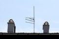 Four TV antennas mounted on strong metal pole on top of suburban family house roof next to two new modern chimneys Royalty Free Stock Photo