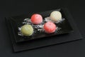 Four types of Japanese dessert mochi - pomegranate with honey, green matcha tea, strawberry, coconut on a black plate on a black