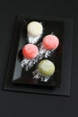 Four types of Japanese dessert mochi - pomegranate with honey, green matcha tea, strawberry, coconut on a black plate