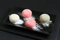 Four types of Japanese dessert mochi - pomegranate with honey, green matcha tea, strawberry, coconut on a black plate on a black