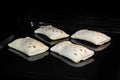 Four uncooked homemade buns on tray in electric oven, black background