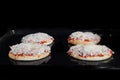 Four uncooked mini pizzas on tray in electric oven: front view, black background