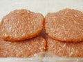 Four uncooked raw turkey burgers with red barbeque flavoring in a plastic packaging on a white simple table cloth. Close up