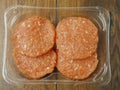 Four uncooked raw turkey burgers with red barbeque flavoring in a plastic packaging on a wooden table. Top view