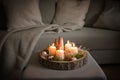 Four white advent candles and Christmas decoration in a rustic tree tray on an ottoman at a couch, cozy winter home decor in the Royalty Free Stock Photo