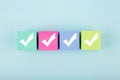 Four white checkmarks on multicolored cubes in a row against bright pastel blue background