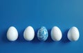 Four white eggs and one blue swirled egg sit in a row on a bright blue background. This is a simple, clean composition perfect Royalty Free Stock Photo