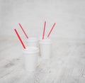 Four white paper cups with red tubes for coffee to go on white wooden table in selective focus Royalty Free Stock Photo