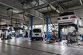 Four white used cars with an open hood raised on a lift for repairing the chassis and engine in a vehicle repair shop. Auto