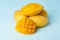 Four whole mango fruits on bright blue table and cut into slices. Large juicy yellow fruits