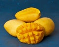 Four whole mango fruits on dark blue table and cut into slices. Large juicy ripe yellow fruits