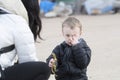 Four Year Old Boy Holding a Dinosaur on a Beach in Winter with Sand in Eye. Mom looking on Royalty Free Stock Photo