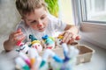 A four-year-old boy with a painted face lying on the windowsill puts eggs decorated for Easter in a craft box Royalty Free Stock Photo
