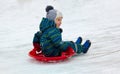 A four-year-old child, a boy, riding a sled from a snow slide.