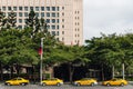 Four yellow taxis waiting for customers along the street that near the park with trees and building in the background in Taipei.