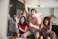 Four young adult friends watching sports on TV celebrating