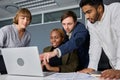 Four young adults in businesswear talking and gesturing while working on laptop at desk in office Royalty Free Stock Photo