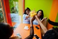 Four young african girls cheers with orange juices while sitting in bright colored fast food restaurant