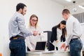 Four young business people working as a team gathered around laptop computer in an open plan modern office Royalty Free Stock Photo