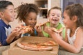 Four young children indoors eating pizza