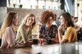 Four Young Female Friends Meeting Sit At Table In Coffee Shop And Talk