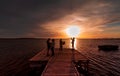 Four young guys and girls taking a picture of the sunset on the water with a smart phone, from a wood pier