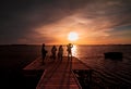 Four young guys and girls taking a picture of the sunset on the water with a smart phone, from a wood pier