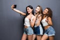 Four young women taking selfie at camera, posing on white studio background in white casual t-shirts and skinny jeans
