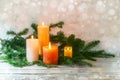 Fourth Advent, arrangement with four candles in orange and yellow, all are lit with a flame, fir branches on light rustic wood,