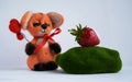 Fox in the hands holds a balloon heart made of wool handmade. He looks at the strawberry lying on the moss.