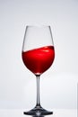 Fragile elegant wineglass of red wine standing against light background.