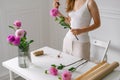 Fragile female florist collects bouquet of pink dahlias in a vase at white table. An image for your floral design