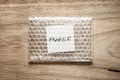 Fragile, handwriting on white squre paper in bubble pack, rought wood background