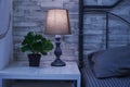 Fragment of a bedroom with a bedside table and a bed. A table lamp and a houseplant are on the nightstand