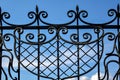 Fragment of black openwork wrought-iron fence grating against blue sky background. Close-up. Copy space.