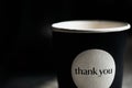 Fragment of black paper cup with the inscription thank you in black blurred background. Close up