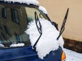 Fragment of a blue car with raised wipers and snow on the windshield