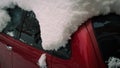 Fragment of a body with glazing of a red passenger car covered with a thick layer of snow.