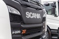 Fragment of the cab of the new Scania P220 XT truck. Scania logo and model number on the front of the vehicle. A close