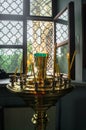 An opened latticed window and a gilt candle holder with burning and extinguished wax candles in the Orthodox Christian church. Royalty Free Stock Photo