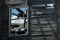 Fragment of the destroyed burned wooden house wall and window. Remains of the structure. View through the window