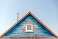 Fragment of facade of wooden house with cracked weathered blue paint, with iron pipe on roof and plastic window with white frame