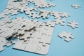 Fragment of a folded white jigsaw puzzle and a pile of uncombed puzzle elements against the background of a blue surface Royalty Free Stock Photo