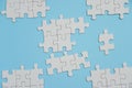 Fragment of a folded white jigsaw puzzle and a pile of uncombed puzzle elements against the background of a blue surface Royalty Free Stock Photo