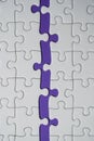 Fragment of a folded white jigsaw puzzle and a pile of uncombed puzzle elements against the background of a Violet surface